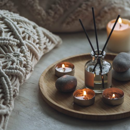 Apartment natural aroma diffusor with sea breeze fragrance. Burning candles on bamboo tray, cozy home atmosphere. Relaxation, detention zone in the living or bedroom. Stones as decor
